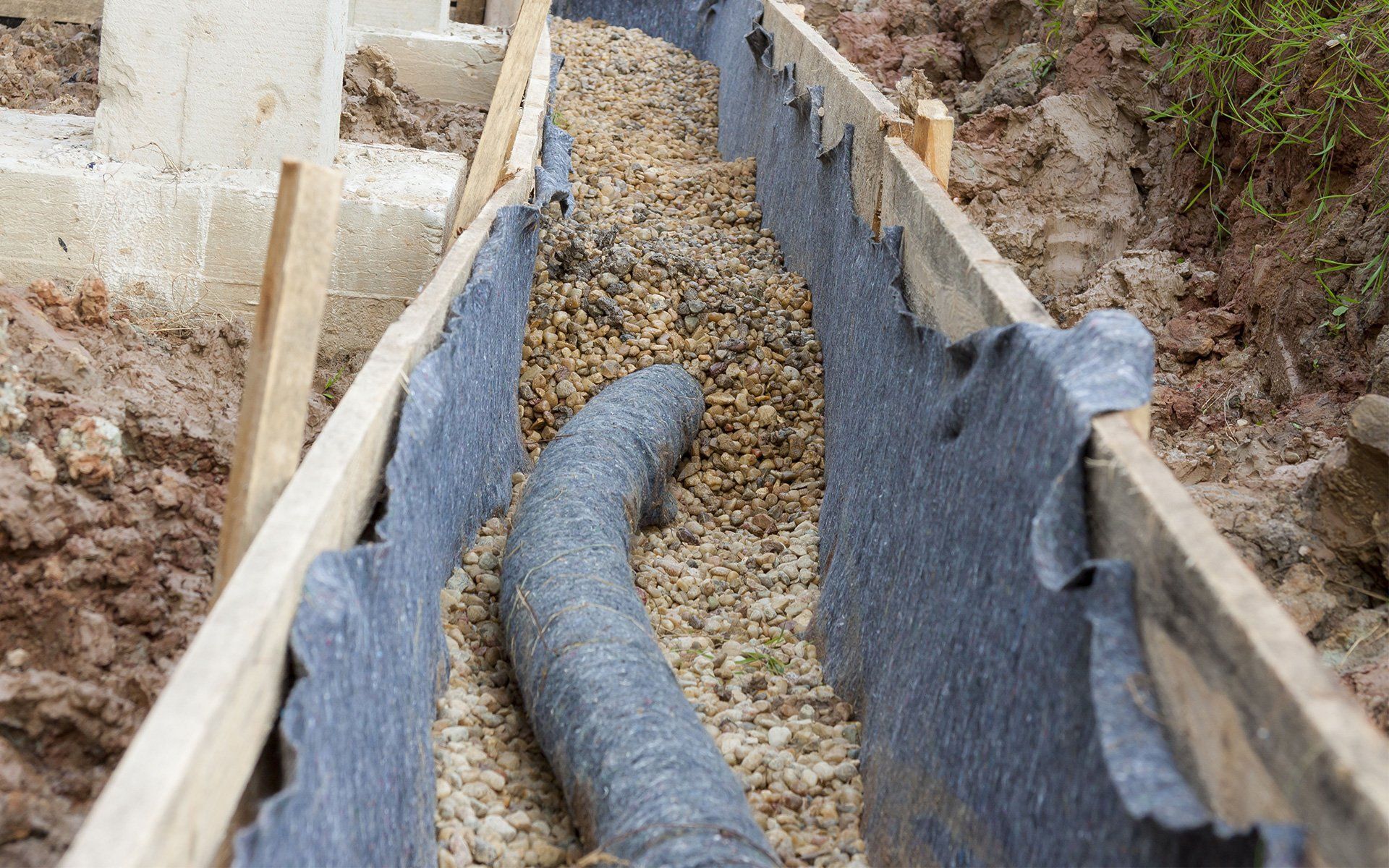 French drain trench with fabric-wrapped pipe running beside a Waco foundation