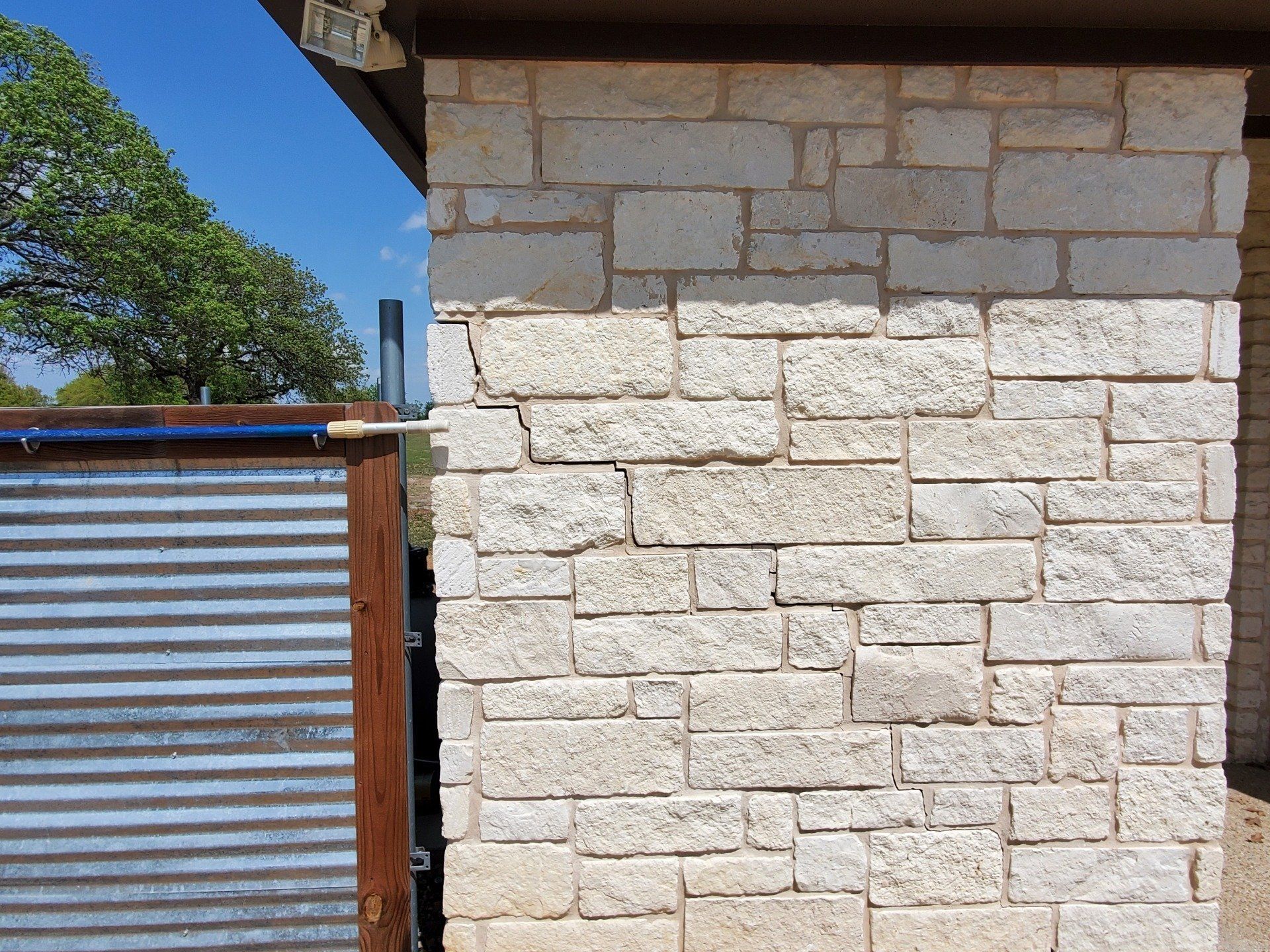 Stair-step crack climbing the limestone veneer at a house corner